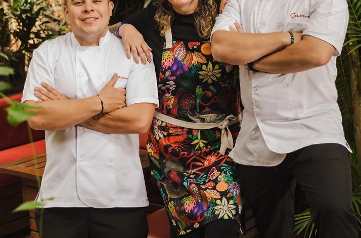 Carmen Ángel and two chefs standing arms-crossed among tropical palms in Carmen Medellín restaurant's outdoor courtyard.