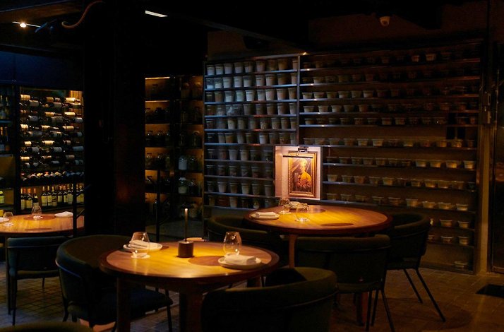 El Chato - The dimly lit dining room — wood tables, wine wall and shelves of ferments