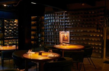 El Chato - The dimly lit dining room — wood tables, wine wall and shelves of ferments