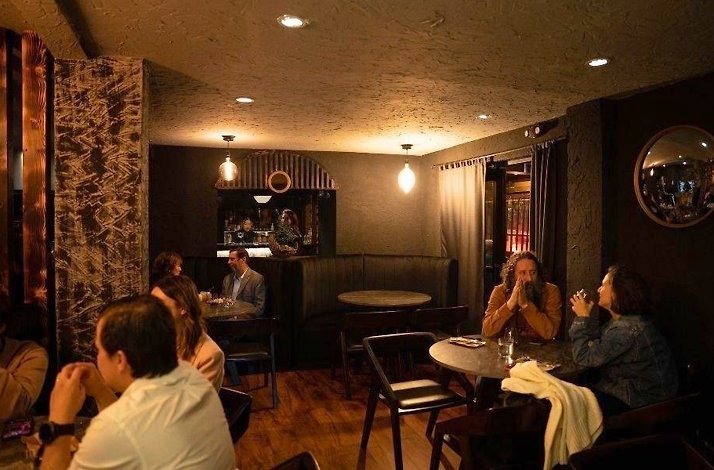 Dimly lit dining room at Humo Negro in Chapinero, Bogotá, with diners at low tables, warm pendant lighting and dark charred-wood textures