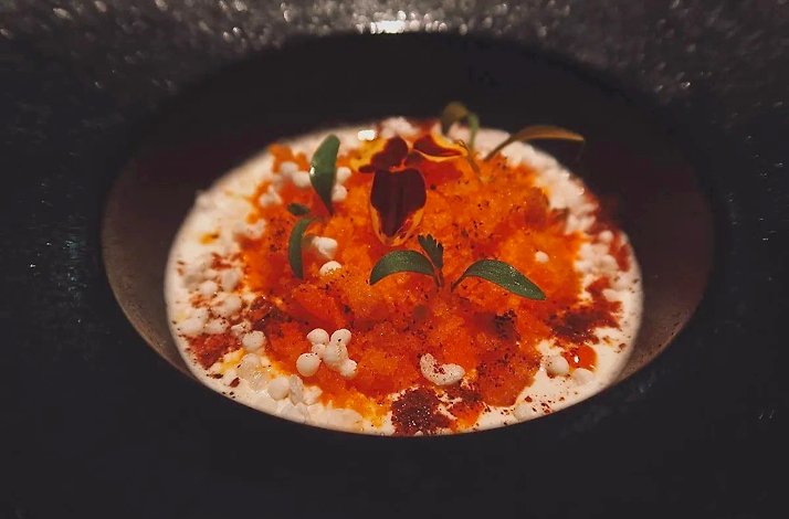 A plated tasting-menu course at Restaurante Leo in Bogotá, Colombia: orange and red garnishes with herbs over a pearled white base, served in a dark bowl.