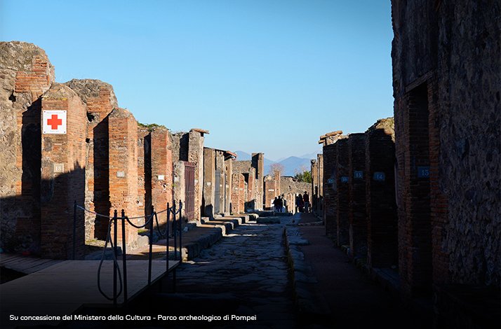 Tourists walking between ancient brick and stone ruins in cobblestone street in Pompeii, Italy.