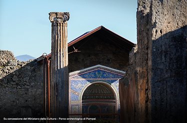 Mosaic fountain in the Casa degli Scienziati, Pompeii, Italy, seen behind a fluted stone column with an Ionic capital.