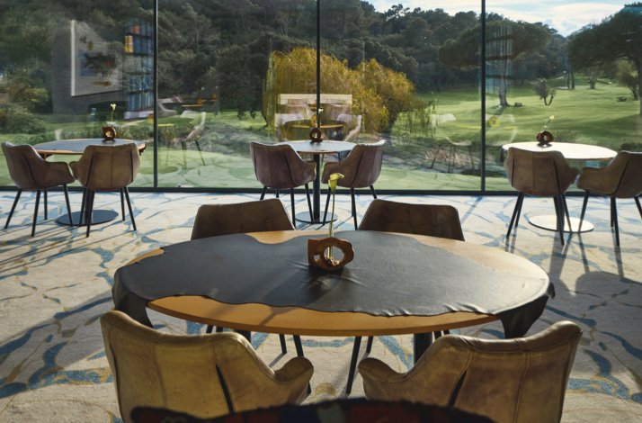 Modern dining area with round tables and chairs, overlooking green gardens through floor-to-ceiling windows at Michelin-starred LAB by Sergi Arola.