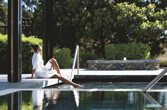 Person in a white robe relaxing at the edge of a tranquil outdoor spa pool, surrounded by greenery at Penha Longa Resort.