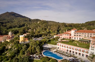 Aerial view of Penha Longa Resort, featuring pink buildings, a pool, and lush green hills within Sintra's natural park.