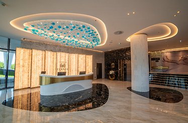 Elegant hotel lobby at Elania Resort & Spa with gold-accented front desk, Logo of Elania centered above it, and glowing oval ceiling artwork.