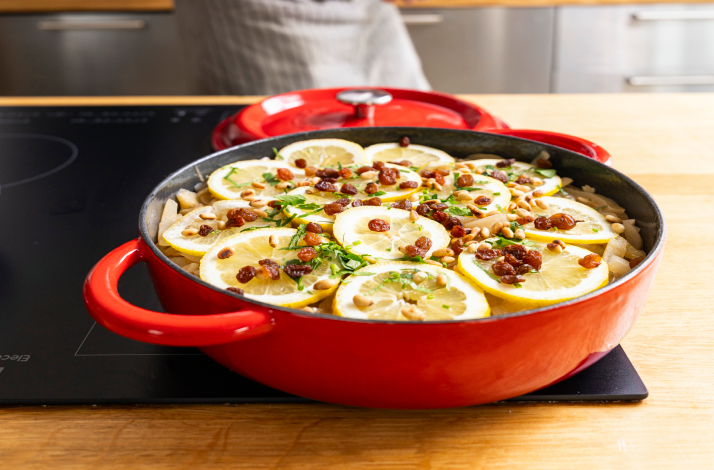 Freshly cooked Dalmatian marinated fish in red pan, decorated with lemon slices, raisins and nuts on top.