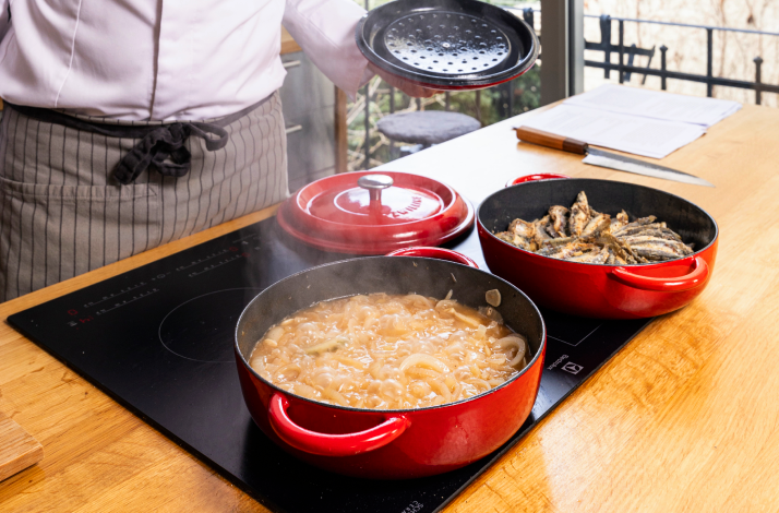 Chef cooking ingredients in two separate red pans on induction hob.