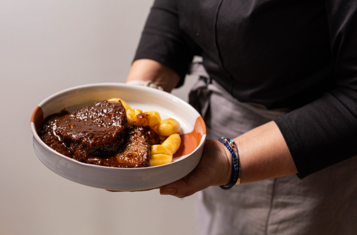 Chef holding a bowl of Dalmatian pašticada with braised beef slices and golden gnocchi in rich dark sauce.