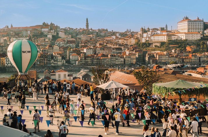 Large crowd attending an outdoor festival at The Wine Experience - Wine Museum, with colorful bunting, market stalls, and Porto's historic skyline.