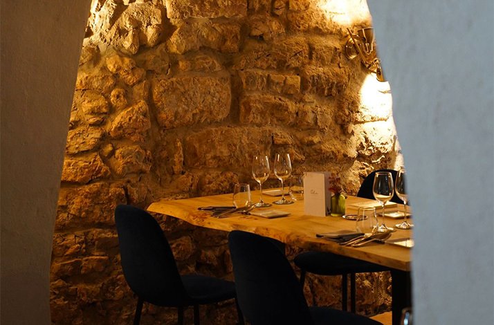 An intimate dining table set against a rustic stone wall inside L'Ogustin restaurant.