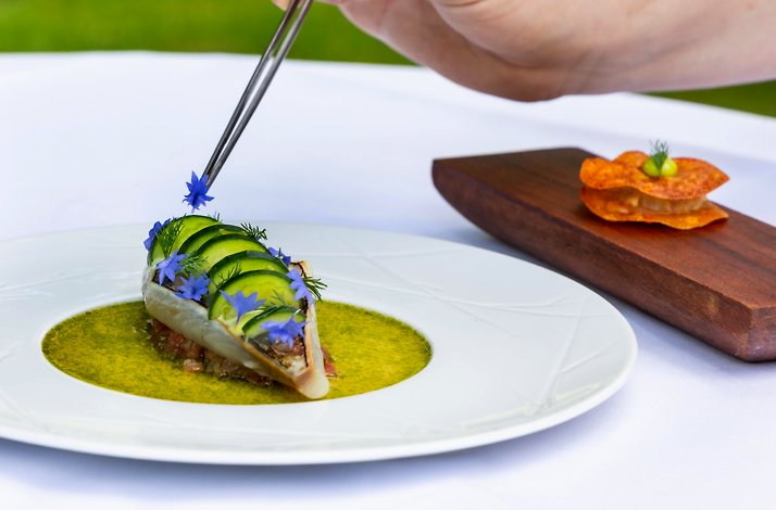 A chef plating a fine dining dish with edible blue flowers at Landhuishotel De Bloemenbeek in the Netherlands.
