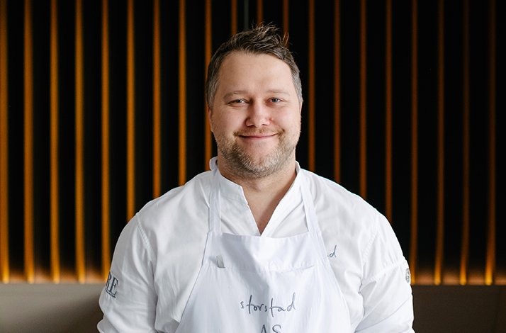Chef Anton Schmaus smiling in a white apron at Storstad restaurant in Regensburg, Germany.