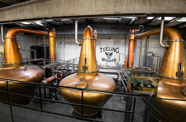 Three large copper pot stills on the production floor at Teeling Whiskey Distillery, with 'Teeling Whiskey' painted on the wall.