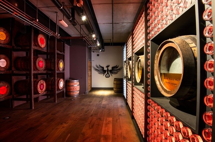 Teeling Whiskey maturation room displaying oak barrels on shelves, whiskey glasses lining the walls, and a phoenix logo mural.