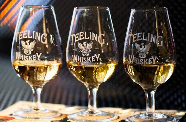 Three Teeling Whiskey tasting glasses filled with amber whiskey, set against a dark background.