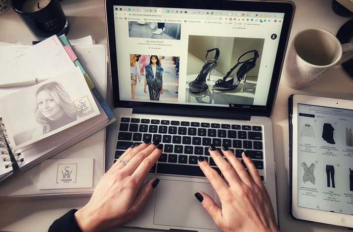 A pair of hands on a laptop crafting a moodboard with a black high heels and a black outfit on a model