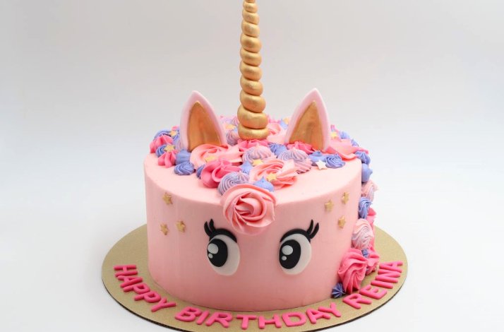 Birthday cake decorated like a unicorn with 2 eyes on the side, a gold horn attached on top and piping that resembles the mane of the unicorn 