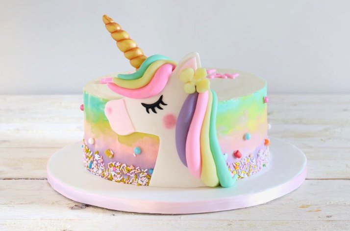 A cake coated with yellow, pink and green frosting with a unicorn icing decorated at the side