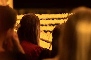 Audience members seated among glowing candles at a Candlelight tribute concert to Coldplay and Imagine Dragons.