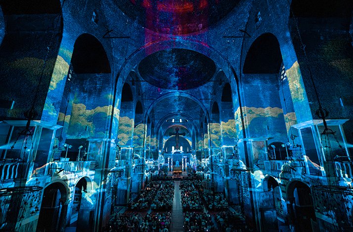 Audience watching vaulted ceiling and arches lit up with multicolored projections at a Luminiscense event.