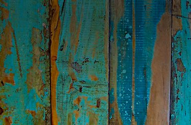 99 Restaurante - Close-up of weathered vertical wooden planks with worn turquoise paint peeling away to reveal the natural brown wood grain beneath.