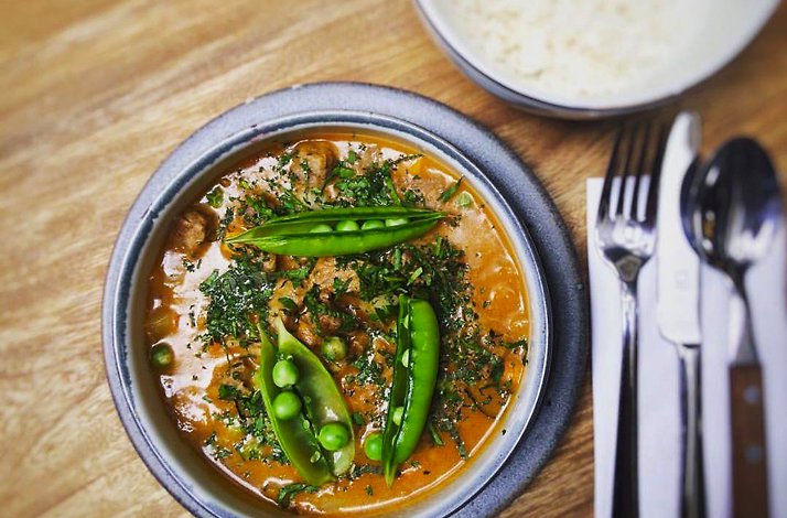 Plated dish at Mesa Franca, Bogotá, Colombia — a braised beef stew in a stoneware bowl garnished with fresh peas and herbs, served with a side of white rice on a wood table
