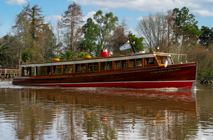 Classic wooden riverboat with an Argentine flag cruising along the water, surrounded by greenery.