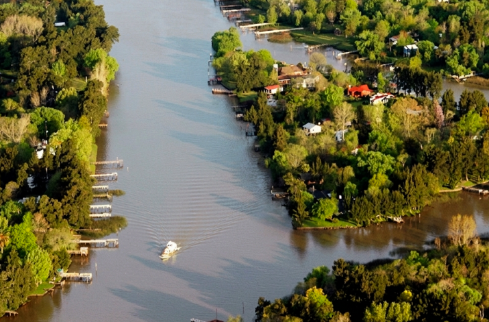 Aerial view of the Tigre River Delta, showing winding waterways, docks, and houses nestled among dense green trees.