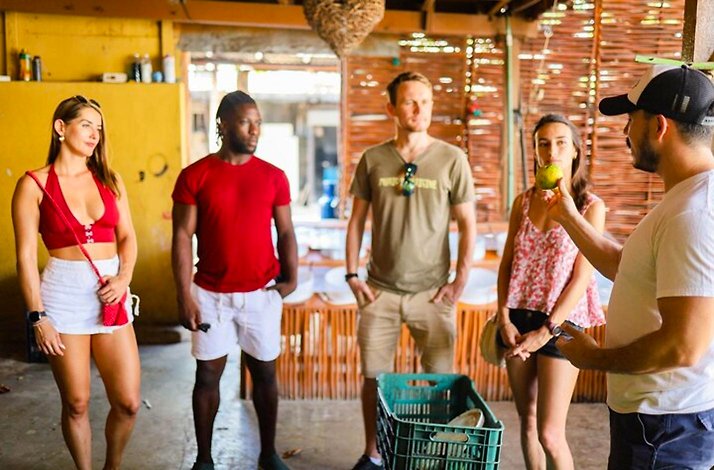 Group listening to a guide holding fresh fruit while learning about local ingredients inside a rustic Playa del Carmen eatery.