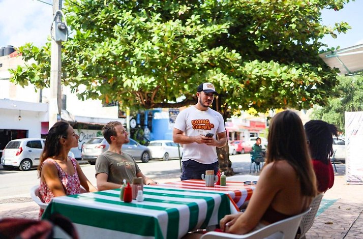 Travelers enjoying a tasting of local tropical fruit drinks at a vibrant market bar in Playa del Carmen during a Caribbean food tour.