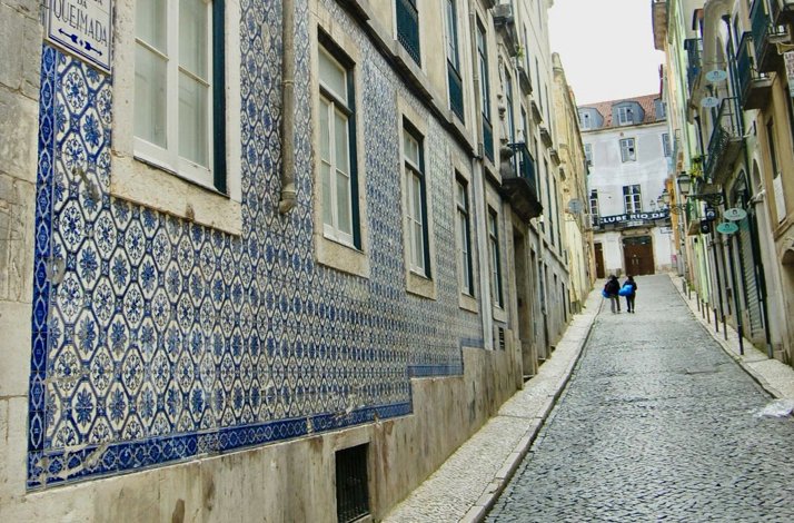 Historic cobblestone street in Lisbon's Bairro Alto lined with traditional blue-and-white azulejo tiles.