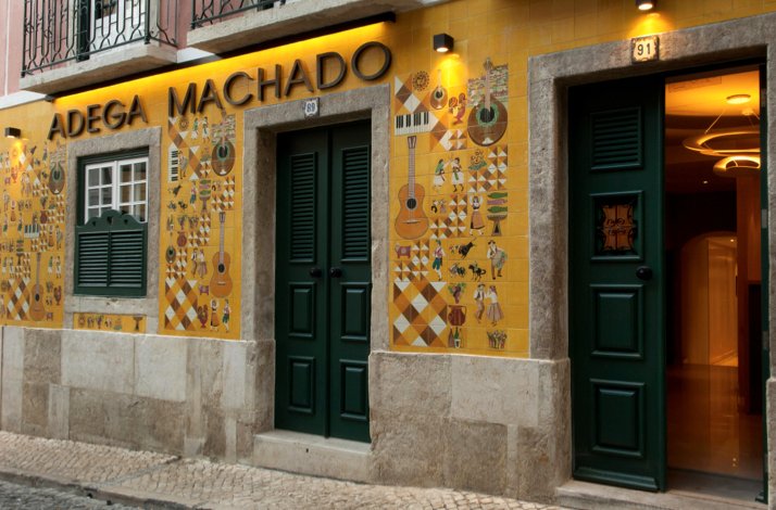 Yellow facade of Adega Machado in Lisbon, Portugal, featuring green doors and traditional music illustrations.