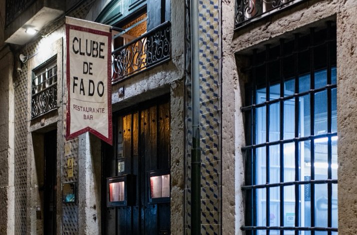 Street-facing entrance of Clube de Fado, Lisbon, with a hanging sign reading 'Clube de Fado Restaurante Bar.'
