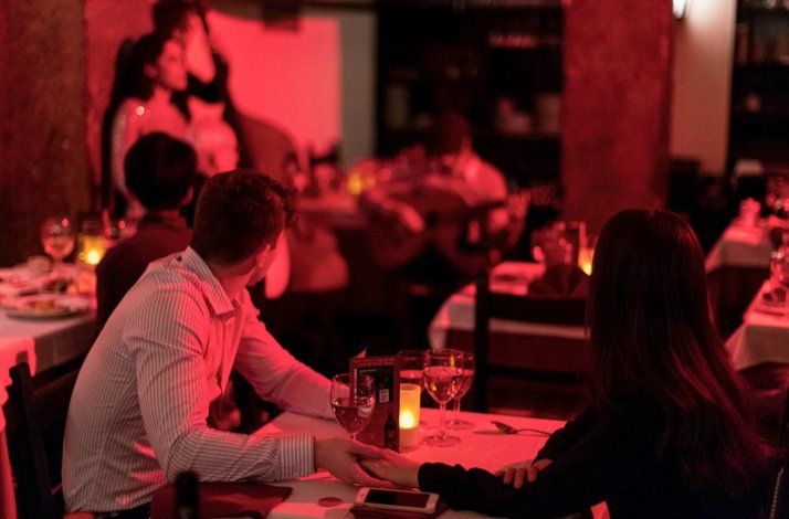 Diners seated at candlelit tables at Clube de Fado, Lisbon, with a guitarist performing in the background.