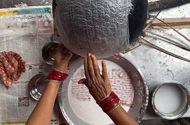Hands adorned with red bangles shaping a textured craft object over a white-pigmented plate, part of a traditional Andhra artisan process.