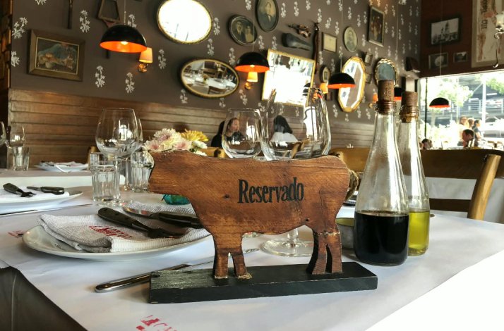 La Cabrera Manila dining table set with wine glasses and a wooden cow-shaped 'Reservado' sign, surrounded by eclectic wall decor.