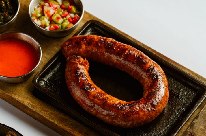 Grilled chorizo sausage coiled on a cast iron skillet, served with chimichurri, tomato sauce, and pepper salsa. 