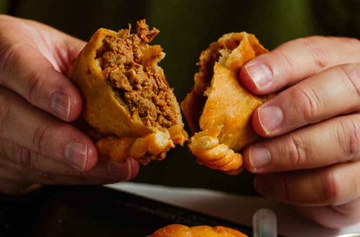 Hands pulling apart a golden fried beef empanada, revealing a shredded meat filling, at Parrilla La Cabrera. 