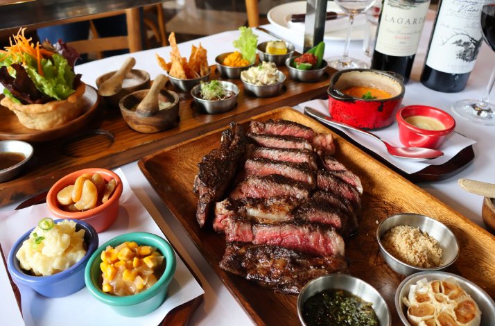 Sliced grilled ribeye served on a wooden board with assorted sides and Zuccardi wine at Parrilla La Cabrera.