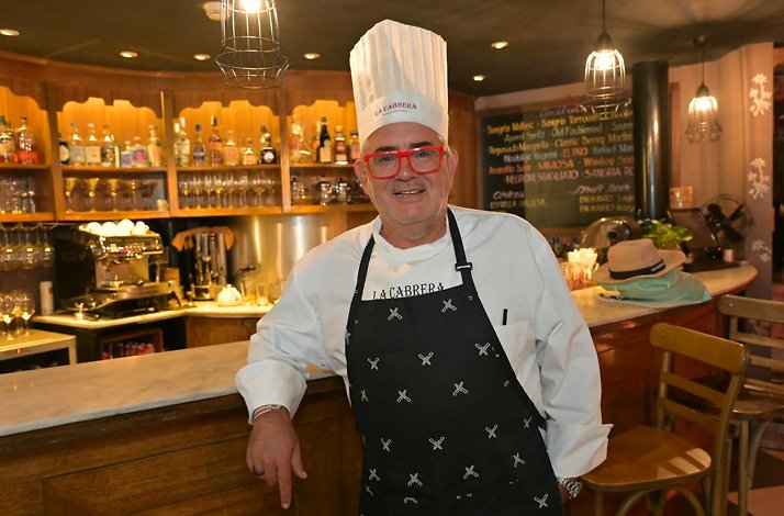 Gaston Riveira wearing a 'La Cabrera'-branded toque and apron, smiling at the bar of La Cabrera Manila.