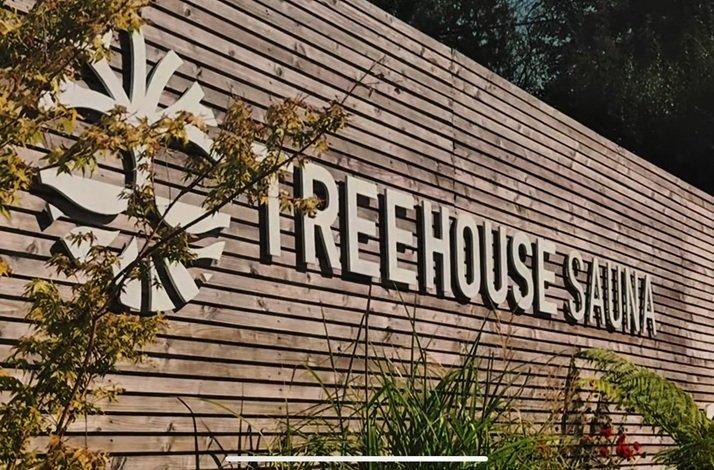 Treehouse Sauna logo on a wooden fence.