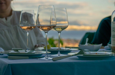 Wine glasses and plates on a table overlooking a sunset over the Adriatic Sea.