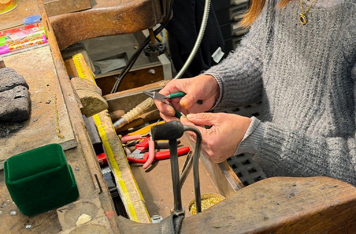 Close-up of a goldsmith working on a delicate piece of jewelry at a wooden workbench.