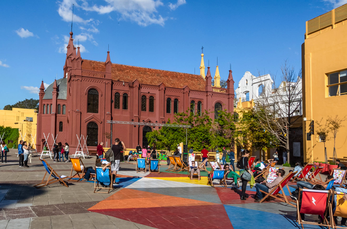 Outdoor plaza in La Boca with locals relaxing on deck chairs near historic buildings under a bright sky.