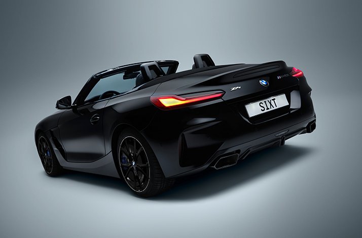 Matte-black BMW Z4 M40i convertible with top down, lit taillights, and a 'SIXT' license plate, part of SIXT's Platinum rental fleet.