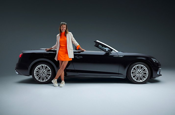 The lady leaning on a black convertible car, as part of a promotional campaign for a rental service SIXT.