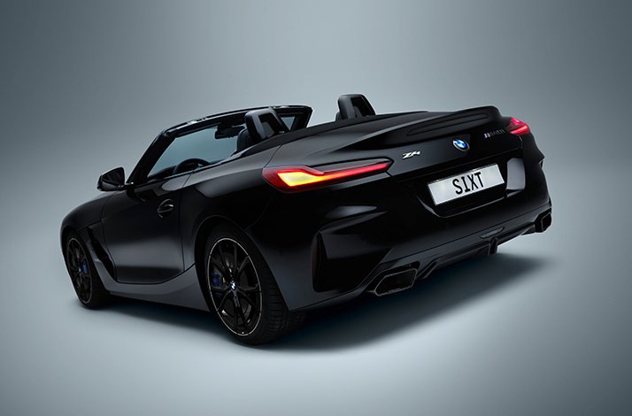 Black BMW Z4 convertible with top down, shown from rear three-quarter angle, bearing 'S1XT' licence plate for SIXT car rental.