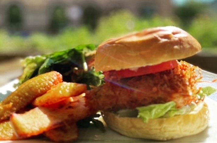 Crispy fried chicken sandwich with tomato and lettuce on a brioche bun, served alongside seasoned fries and a fresh green salad at The Edge Harlem.
